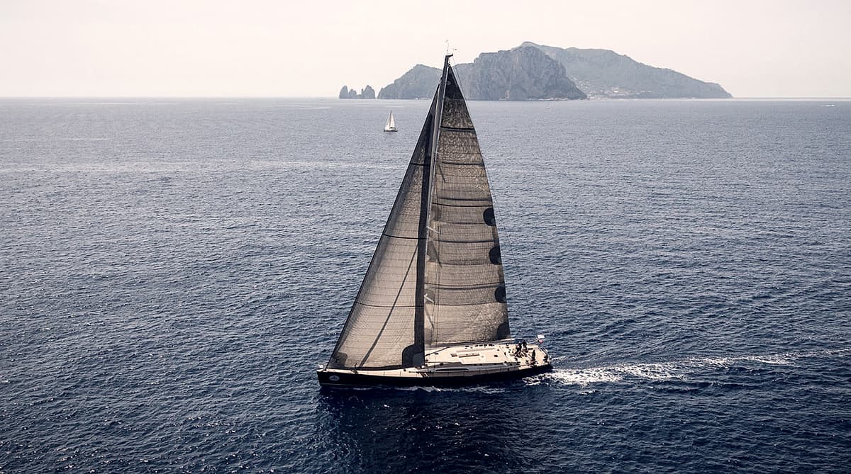 A sailing yacht under full sail off a rocky headland
