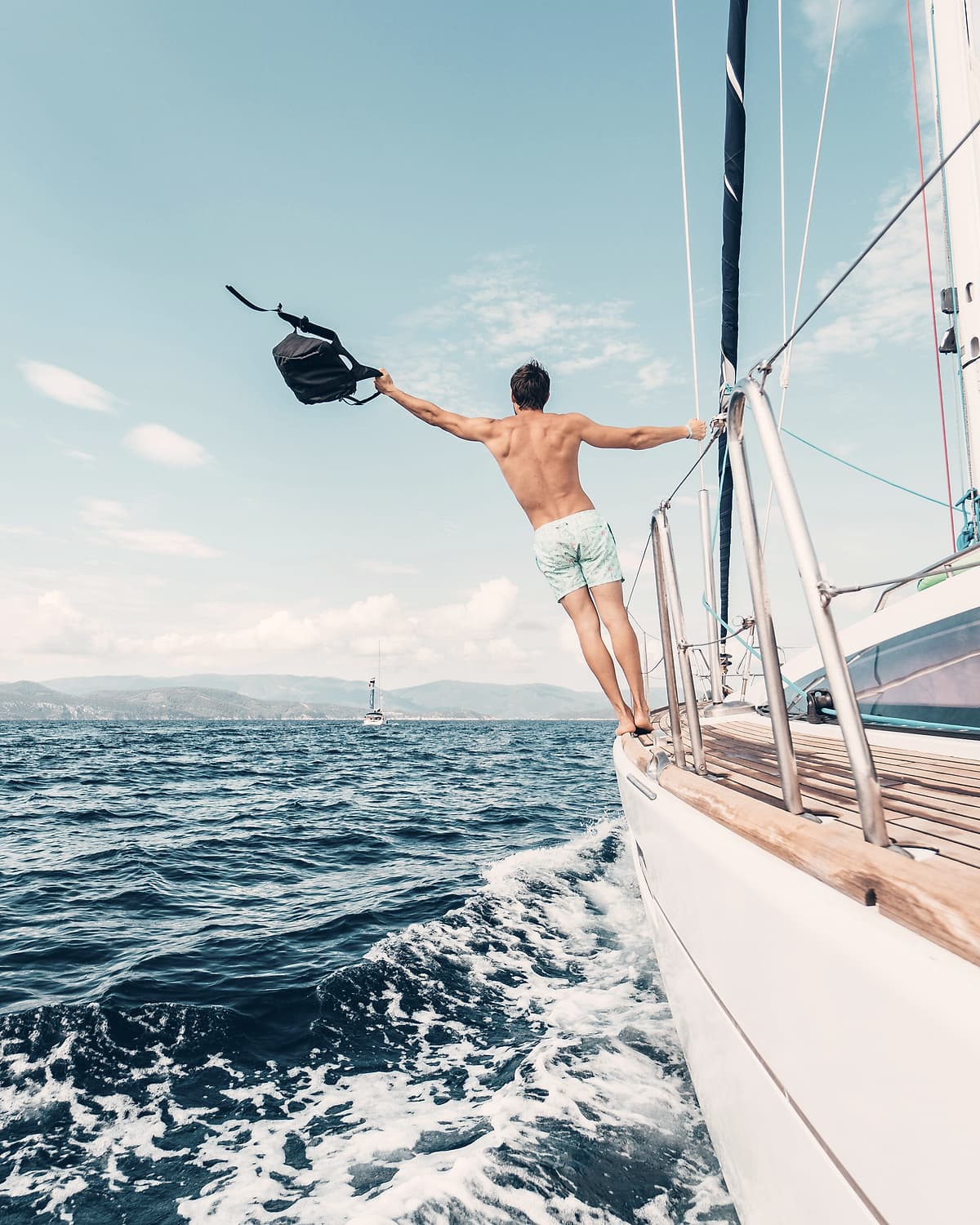 A guest on the bow of a sailing yacht under way, about to jump
