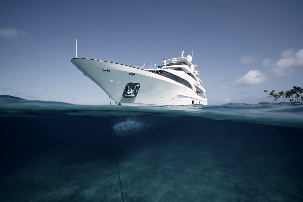 A motor yacht at anchor, seen half above and half below the surface of clear water