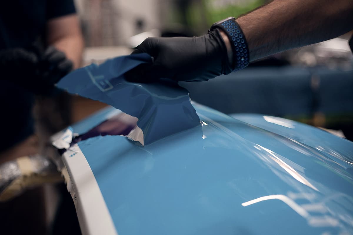 A technician smoothing blue vinyl wrap onto a hull